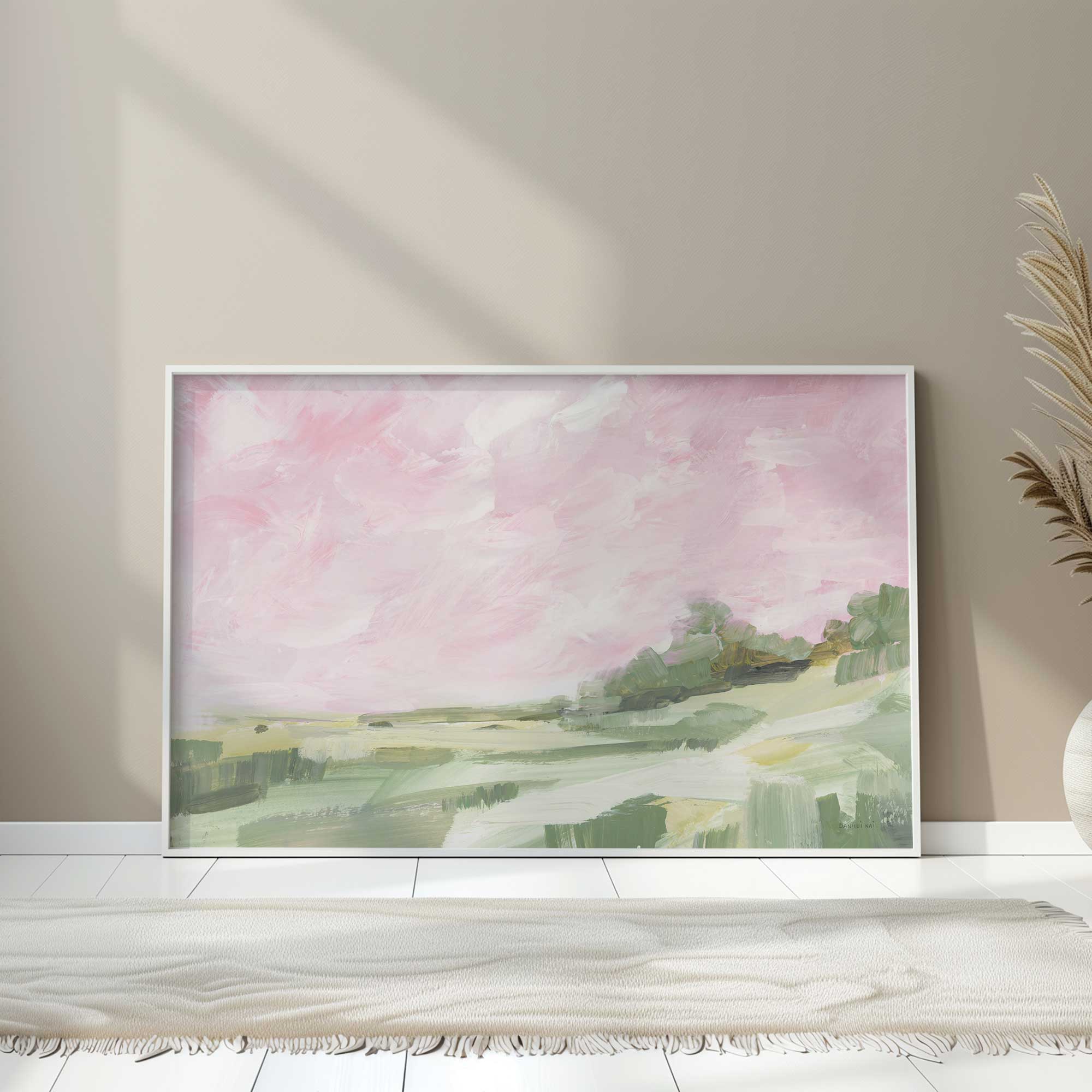 abstract green hillside under soft pink sky art print in a white frame leaning against a wall